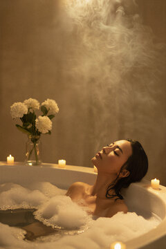 Woman relaxing in candlelit bubble bath with rising steam