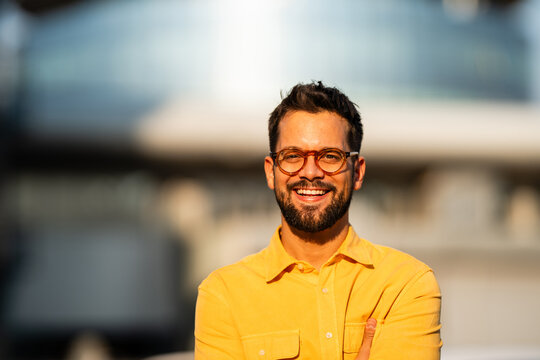 Smiling man wearing glasses standing outdoors with folded arms