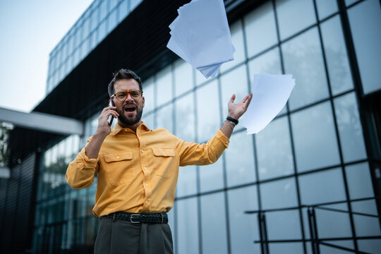 Frustrated businessman shouting on phone call throwing papers