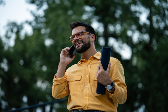 Professional man talking on phone holding blueprints tube