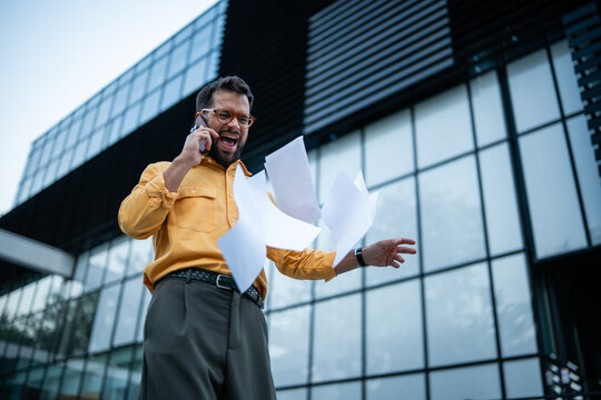 Frustrated businessman throwing documents during phone call