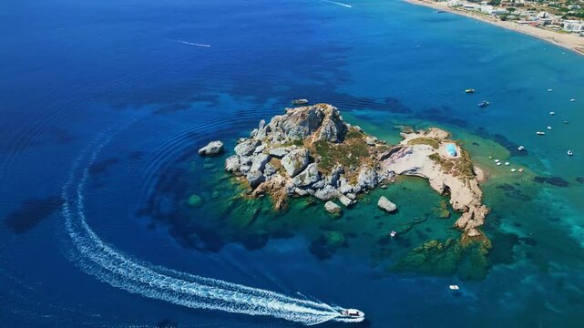 An aerial drone shot showcasing the picturesque rocky islet of Kastri located in Kefalos Bay, opposite Agios Stefanos Beach on Kos Island, Greece. The vibrant turquoise and azure waters of the Aegean 