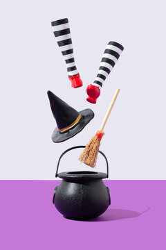 Witch' legs with red shoes, hat, broomstick floating under cauldroun on a white and purple background. Magic holiday concept.