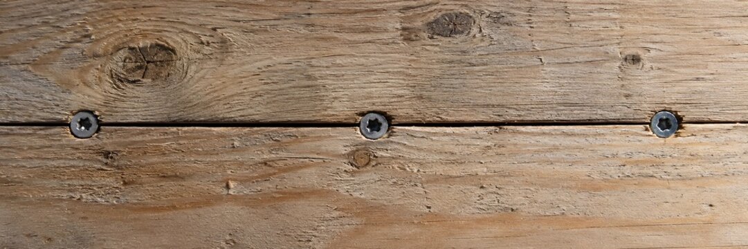Macro panoramic texture of rustic wooden timber decking planks fastened with countersunk steel torx screws displaying natural wood knots and grain fissures