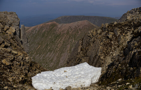 Melting summer snow patch in a steep rocky gully on Ben Nevis, Scotland. Alpine landscape with moss and stones, illustrating high altitude Scottish nature.