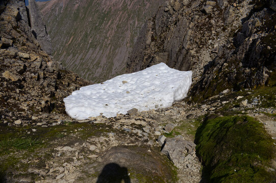 Melting summer snow patch in a steep rocky gully on Ben Nevis, Scotland. Alpine landscape with moss and stones, illustrating high altitude Scottish nature.