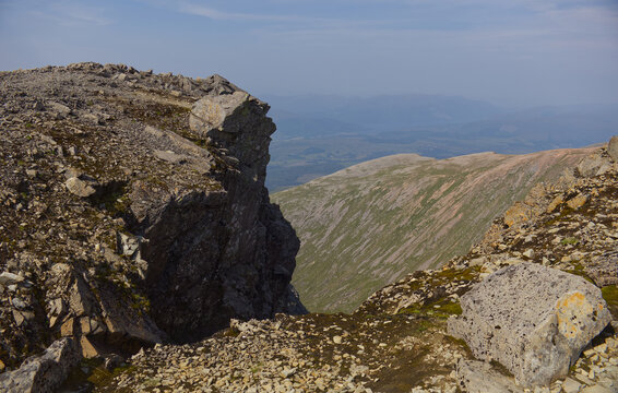 Dramatic steep rocky cliff edge dropping into a deep mountain valley. Dangerous drop-off, rugged Scottish Highlands landscape, extreme nature.
