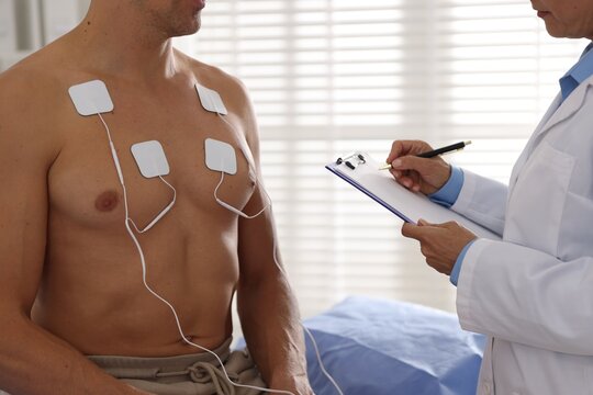 Doctor writing notes during patient's ECG test in clinic, closeup