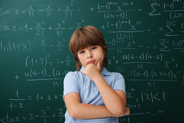 Obraz premium Puzzled student standing by green chalkboard covered with equations. Back to school