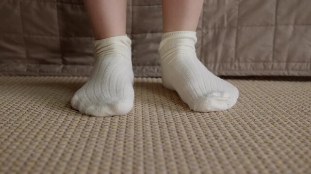 Woman taking off white cotton socks. Close-up view of a young woman's feet as she takes off her white ribbed cotton socks, standing on a textured floor next to her bed