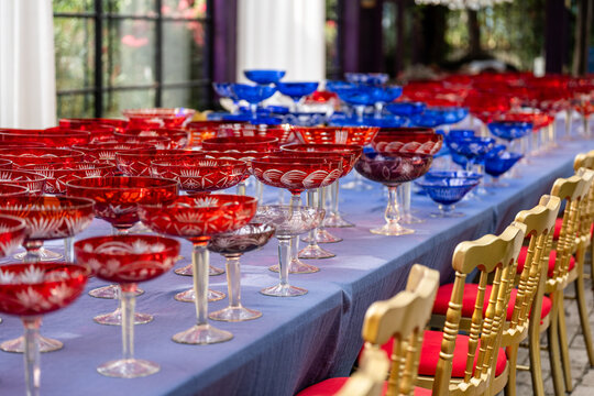 Banquet table with many vintage red and blue crystal glasses, preparations for festive celebrations, catering settings in fancy restaurant with luxury glasses, wedding reception or corporate event.