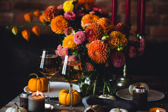 Cozy festive holiday table decor for home family Thanksgiving dinner. Bright dahlias, elegant natural decoration. Wooden rustic table, countryside style. Burning candles, floral centrepiece pumpkin