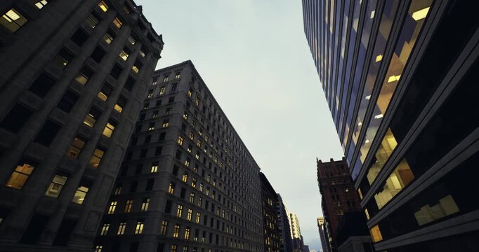 narrow avenue between historic office towers with glowing windows and lamplight, deep perspective lines draw eye toward distant skyline, atmosphere of evening