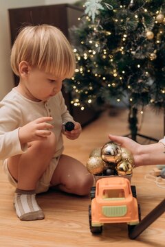 Toddler playing with toy truck full of Christmas ornaments beside glowing tree at home combining family tradition imaginative play fine motor learning childhood curiosity and cozy holiday lifestyle