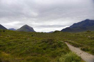Fototapeta premium Hiking trail leading through green moorland towards the dramatic dark peaks of the Black Cuillin mountains on the Isle of Skye, Scotland.