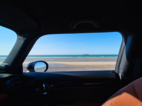 View from a car side window of a beach at low tide with a ship on the horizon. Minimalist summer sea travel landscape.