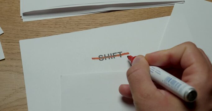 Hand crossing out the word shift with a red pen on paper, representing schedule changes and cancelled work assignments