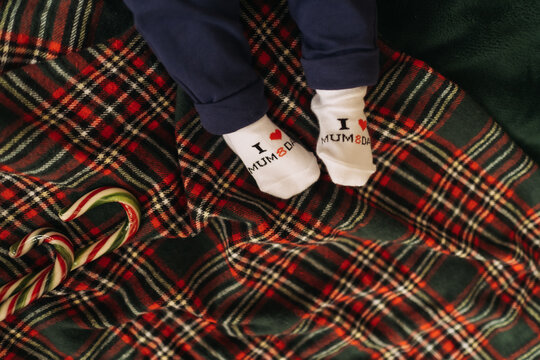 Baby feet in socks on plaid blanket near christmas candy canes.
