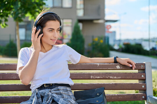 Young woman listening music in headphones outdoors park bench