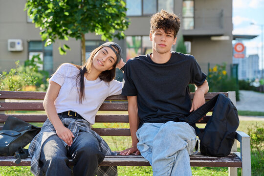Young couple sitting on bench outdoors looking at camera