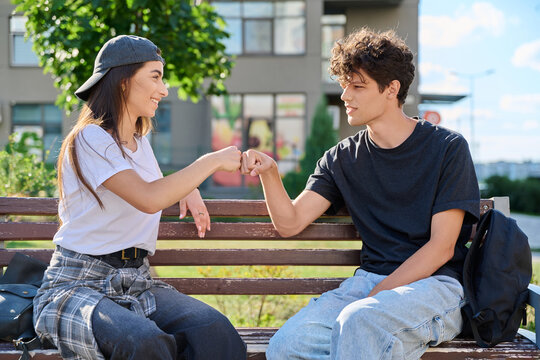 Young man and woman giving fist bump sitting park bench outdoor