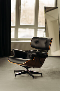 Black leather lounge chair with wooden base in modern interior near window.