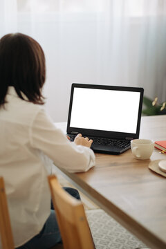 Woman typing on laptop with blank white screen mockup sitting indoors working remotely.