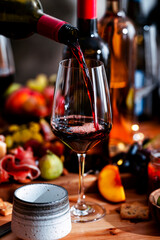Obraz premium Pinot Noir red wine poured from bottle during lunch gathering. Authentic food pairing with rich cheese, prosciutto on table. Sommelier expertise, elegant dining culture and social connection.