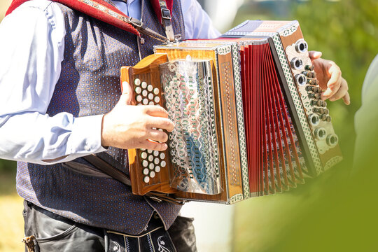 Unrecognizable male musician in traditional Bavarian clothing playing accordion outdoors at a folk festival.