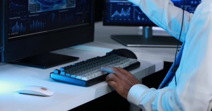 Professional analyst working at a dual monitor desk with financial charts, keyboard and mouse in a modern office.