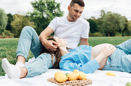 A portrait of an expectant couple relaxing and dreaming together during a picnic on a lemon-yellow blanket in the park on a summer day.