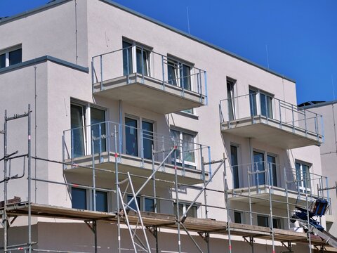 Modern residential apartment building under construction featuring light grey facade finish, steel balcony railings, and scaffolding frame