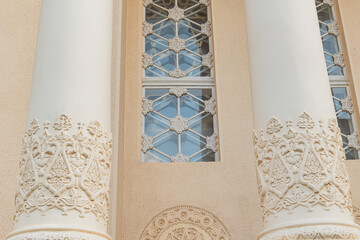 Close-up of ornate columns with floral carvings flanking a decorative window with a geometric grille.   © tatiana
