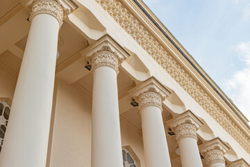 Low-angle view of a building's colonnade with ornate capitals and frieze against a blue sky. © tatiana