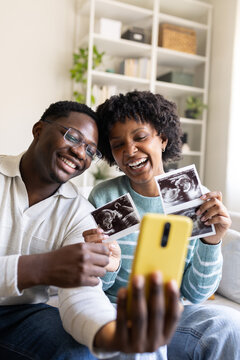 Happy couple sharing ultrasound pictures on video call at home