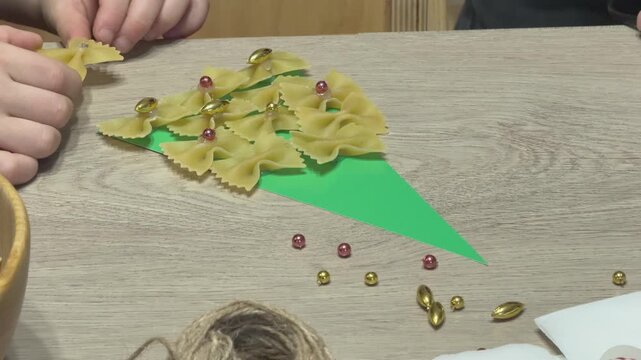  Child prepares craft materials by cutting beads with scissors into bowl. School or kindergarten holiday activity. Suitable for educational, family and DIY seasonal content.