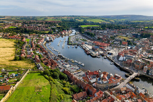 Whitby harbour and River Esk estuary with moored yachts and fishing boats, red tile roofs of the seaside town stretching toward rolling countryside