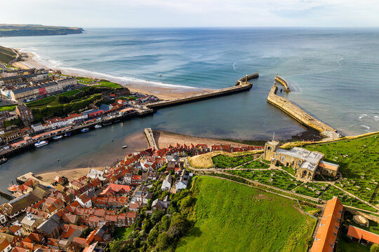 Aerial view of Whitby harbour and town on North Yorkshire coast, historic stone piers extending into North Sea beside St Mary's Church and red-roof houses