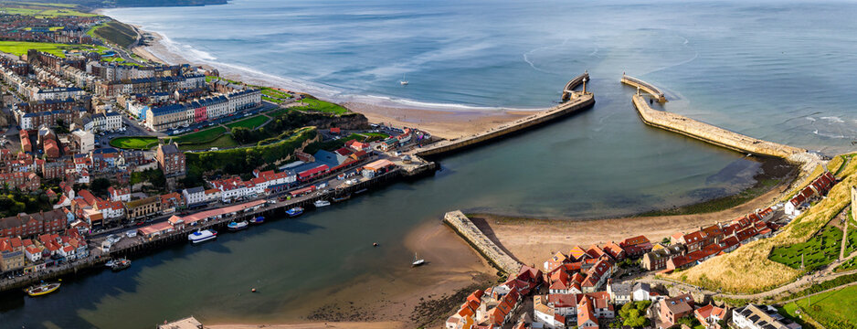 Whitby harbour and stone piers leading into the North Sea, Yorkshire coast, red tiled rooftops, quay and River Esk estuary at low tide, aerial view