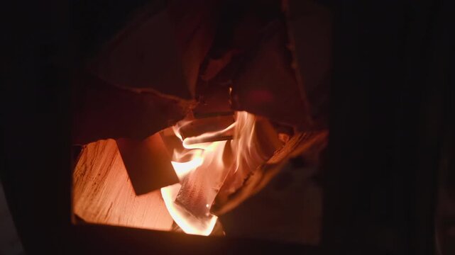 Bright flame rises inside dark stove opening with wooden logs glowing in warm orange light, creating strong contrast, dramatic shadows, and confined rustic fire scene with active burning motion