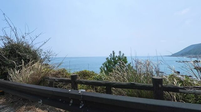 Calm sea and a distant headland behind a rustic fence and wild grass