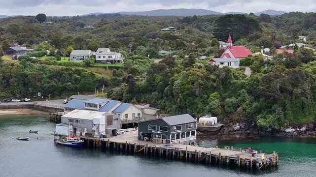 Aerial landscape view, panning left across Halfmoon Bay in Oban, a settlement on Stewart Island, New Zealand, from Ferry Terminal along beach and hilly wooded landscape - 4k aerial video