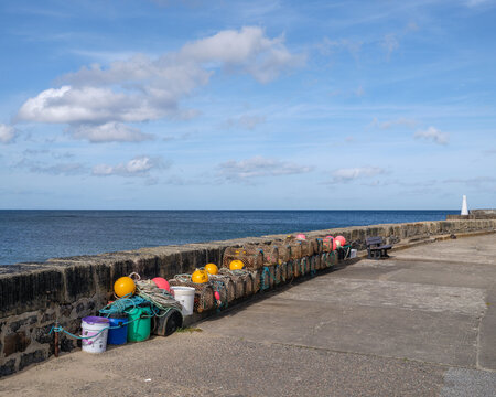 Fishing creels stacked along the stone pier at Cullen Harbour in Moray Scotland under a clear blue sky on a bright sunny day during the afternoon