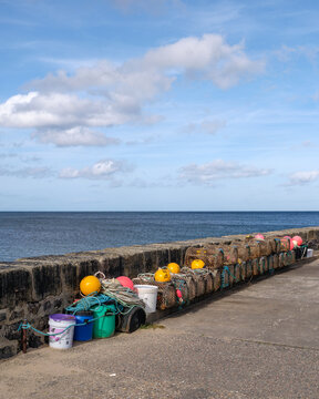 Fishing creels stacked along the historic Cullen Harbour Pier located in Moray Scotland under a bright blue sky during a calm day of activity