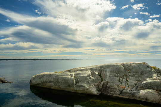 Dramatic glacier-scoured granite rock beneath a wide cloud-filled sky on calm water with copy space, Bustard Rocks, Georgian Bay, Ontario, Canada