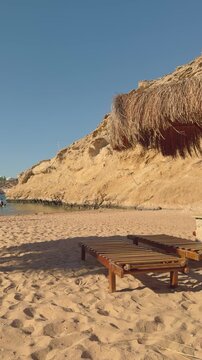 Relaxing beach scene with wooden loungers by cliffs and straw umbrella
