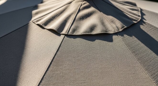 Close up of a beige outdoor umbrella fabric texture with sunlight and shadow showing pleats and details