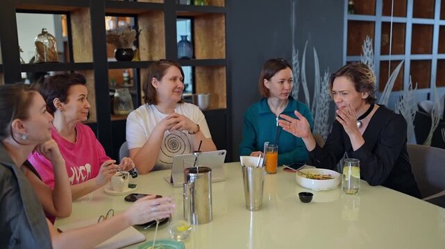 Six professional women seated around round table in modern conference lounge with warm lighting and glass partition