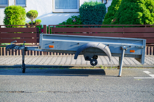 Damaged utility trailer with missing wheels parked on residential street in daylight