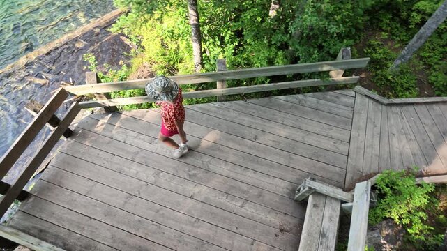 Young person standing on boardwalk, looking down at turquoise water of Olive Lake, revealing submerged logs and rocks through transparent surface in Kootenay National Park in British Columbia, Canada